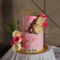A lovely two-tier anniversary cake in shades of pink, decorated with fresh pink and white roses and a touch of gold leaf. This design is perfect for celebrating love with elegance.