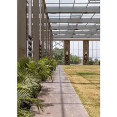 The design ensures a seamless transition between the built structure and the natural earth. A row of indoor plants lines the edge, further softening the boundary between the interior lawn and the glass enclosure.
