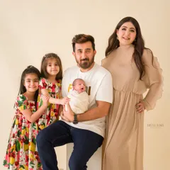 A beautiful portrait of a family welcoming their newest member. The older sisters proudly stand with their parents and new baby brother.