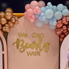 This teddy bear themed baby shower backdrop says "We Can Bearly Wait" in gold lettering. I used an organic balloon garland with pink, blue, and metallic balloons to frame the custom-designed wall.