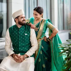 A full-length view of the coordinated couple, showcasing how the bride's elegant saree and the groom's smart traditional wear come together. The styling ensures they look connected and perfectly matched for their special day.