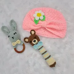 A collection of baby items, including a pink turban-style hat, a bear rattle, and a bunny rattle.