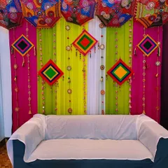 A festive Mehendi backdrop with colorful drapes in pink and lime green, adorned with traditional Rajasthani umbrellas.