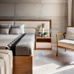 The guest bedroom at Noor Haus features a striking contrast between raw, concrete-finish wall panels and the warmth of the wooden bed frame. The design is minimal, peaceful, and perfectly balanced.