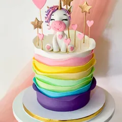 This unicorn cake features wavy, petal-like layers of rainbow buttercream. The cheerful unicorn topper is surrounded by fondant hearts and stars.