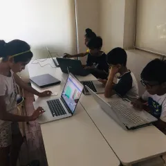 Students deeply engaged in building their projects during a summer coding camp. Each child works on their own laptop, bringing their unique ideas for games and apps to life.