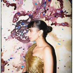 A profile shot against an artistic backdrop, highlighting the texture of the antique gold sculpted top.