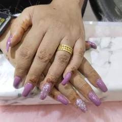 A full set of long, square-shaped extensions in a solid mauve-purple color. To add some glamour, the ring finger on each hand is coated in a dense, sparkling silver glitter. This is a great way to elevate a simple color.