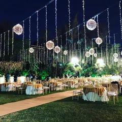 I create magical evening atmospheres for outdoor events using strategic lighting. Here, hanging fairy lights and illuminated globes cast a warm glow over the entire lawn, transforming the space into a royal and majestic setting for a corporate reception.