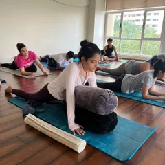 A student uses multiple bolsters to ease into a deep hip-opening stretch, allowing for a longer, more restorative hold.