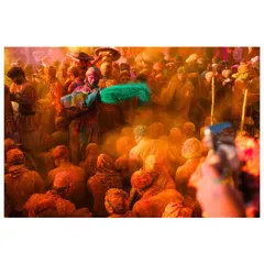 A moment of pure chaos and color during Holi celebrations. A cloud of orange and a splash of green powder fill the air as people celebrate together in a dense crowd.