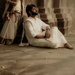 A thoughtful, artistic shot of the groom resting against ancient temple steps. The composition, with his partner just in frame, tells a story of shared peace and companionship.