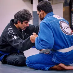 Two practitioners engage in a technical grip fight during a Gi jiu-jitsu session. Mastering the Gi allows you to control your opponent's posture and set up submissions, a key skill in traditional BJJ.