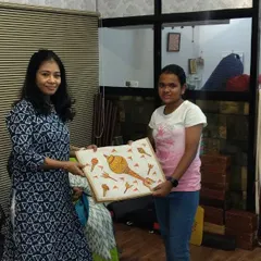 Siya, a 7th standard student, receives her completed tote bag. She painted a traditional conch shell design using acrylics on the jute material.