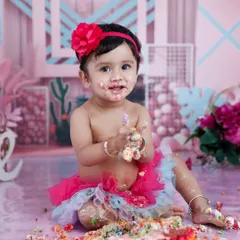 A colorful and messy cakesmash photo of a baby girl with a rainbow cake. This image captures the fun and spontaneity of a first birthday celebration.