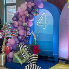 A vibrant and playful decor setup for a 4th birthday party. The mix of purple and blue balloons, a neon number '4', and quirky striped vases shows my creative and eclectic style.