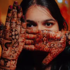 A creative portrait of the bride peeking through her hands, drawing attention to both her eyes and her beautiful mehndi.