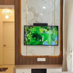 A close-up of a modern TV wall unit. The design combines a fluted wooden panel with a large marble-finish slab, creating a beautiful contrast of textures. The integrated backlighting adds warmth and highlights the materials.