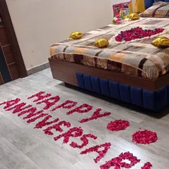 For this anniversary celebration, I spelled out 'HAPPY ANNIVERSARY' on the floor using fresh red rose petals. The bed is also decorated with a floral centerpiece and gold foil balloons to complete the surprise.