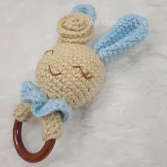 A sleepy bunny baby rattle with a wooden teether ring. The different textures of the yarn and wood are great for a baby's sensory development.