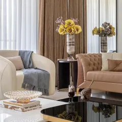 Curated decor and plush furnishings in tones of cream and brown add warmth and texture to the living room. Large windows dressed in dual-layered curtains allow for controlled natural light, enhancing the room's ambient quality.