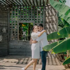A happy, relaxed portrait from a pre-wedding shoot at a resort. The rustic wooden backdrop and lush greenery create a warm and inviting atmosphere.