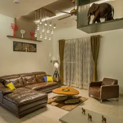 Another view of the living space, highlighting the interplay of different decor elements. A tripod floor lamp adds an industrial touch, while the custom coffee table and shelving with elephant sculptures bring in unique, personal details.