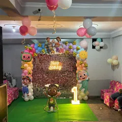 A wide view of a Cocomelon-themed party in a large hall, showing the stage, ceiling decor, and seating area.