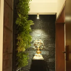 We create tranquil corners by blending nature with art. This vertical garden is paired with a spotlit Buddha statue against a dark, textured wall, creating a focal point of peace and serenity in a modern hallway.