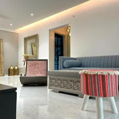 The living area of the Bandra bohemian home, featuring a custom-carved sofa base, a colorful woven stool, and unique accent chairs. The polished terrazzo floor reflects the light, making the space feel bright and open.