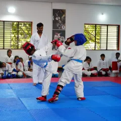 Two of our young students engage in a controlled sparring match during a belt exam, complete with protective gear. We teach competitive karate with a strong emphasis on safety and sportsmanship.