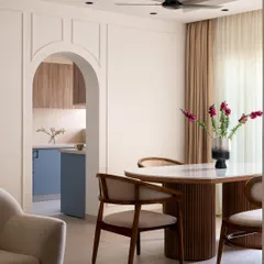 This view shows the dining area and the arched entryway to the kitchen. The fluted wood dining table and cane-back chairs add warmth and texture, creating a cohesive flow from the living space to the kitchen.