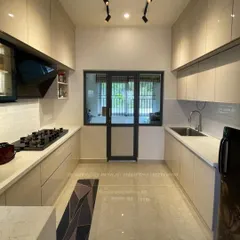 A spacious parallel kitchen with handle-less cabinets in a light beige glossy finish. The layout provides ample counter space and storage, making it highly functional for everyday cooking.