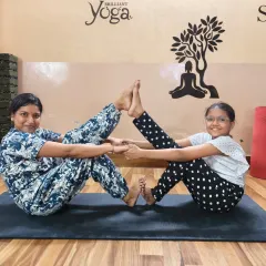 A mother and daughter share a beautiful moment practicing a partner boat pose. Partner yoga is a wonderful activity for families to connect, have fun, and build healthy habits together.