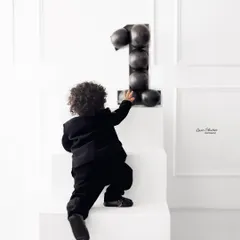 A candid moment from the minimalist first birthday shoot, capturing the little one's curiosity as he reaches for the number one.