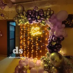 We designed this romantic proposal setup featuring a 'Better Together' neon sign. The backdrop includes a curtain of fairy lights with polaroid-style photos clipped on, framed by a lush balloon arch in shades of purple and chrome.