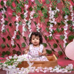 A lovely studio portrait with a pink floral theme. This little girl is sitting in a wooden box, surrounded by a wall of hanging flowers.