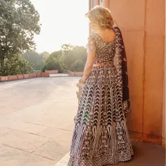 A back view of the model in her ornate lehenga, set against the backdrop of golden hour light. This perspective emphasizes the detailed craftsmanship of the traditional Indian garment.