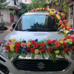 A front view of a wedding car with a garland of multi-colored flowers across the hood and a floral arrangement on the roof.