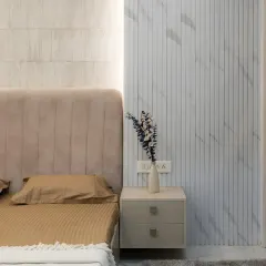This image showcases the beautiful combination of textures in the bedroom, with a soft upholstered headboard placed next to a wall with sleek, marble-finish fluted panels.