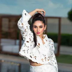 A high-fashion outdoor portrait for a magazine. The pose and high ponytail hairstyle complement the structured, modern design of the white laser-cut outfit.