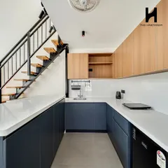 A look at the U-shaped modular kitchen under the mezzanine. The two-tone cabinets in navy and light wood, paired with a white countertop, create a clean and contemporary feel.