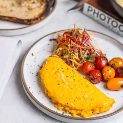 A beautifully folded omelette served with a side of sweet, roasted cherry tomatoes and a vibrant coleslaw. It’s a light yet filling option for those who want a fresh and wholesome start.
