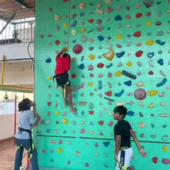Safety is central to everything we do. This image shows our top-rope setup, where young climbers are securely harnessed and supported by a belayer on the ground, allowing them to climb higher with complete confidence.