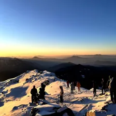 Trekkers at the Kedarkantha summit during sunrise, with layers of Himalayan peaks in the background. This is the reward for an early morning start and a challenging climb.