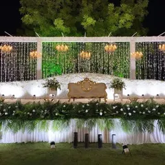 For this outdoor reception, I designed an elegant stage featuring cascading crystal strings, grand chandeliers, and a lush base of white flowers and greenery, creating a magical ambiance under the open sky.