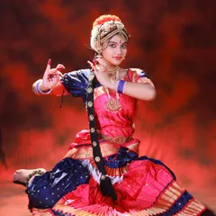 A graceful seated pose showcasing the intricate hand mudras of classical dance. The composition allows the full costume to spread out beautifully.