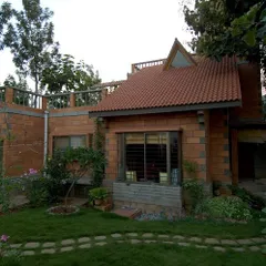 The Sharada Residence, with its sloping tiled roof and integration with the garden, evokes the charm of a traditional cottage. The design prioritizes a human scale and a strong connection to the natural surroundings.