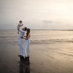 A classic family pose against the setting sun. The father lifts their child high in the air, creating a beautiful silhouette and a memory filled with pure happiness.