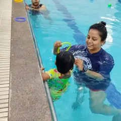 A coach uses a toy to engage a toddler in the water, making learning a playful experience.